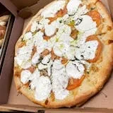 A whole pizza with large white cheese blobs and red tomato slices.