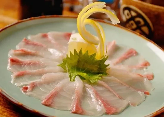 Thinly sliced raw white fish, garnished with lemon and green leaf.