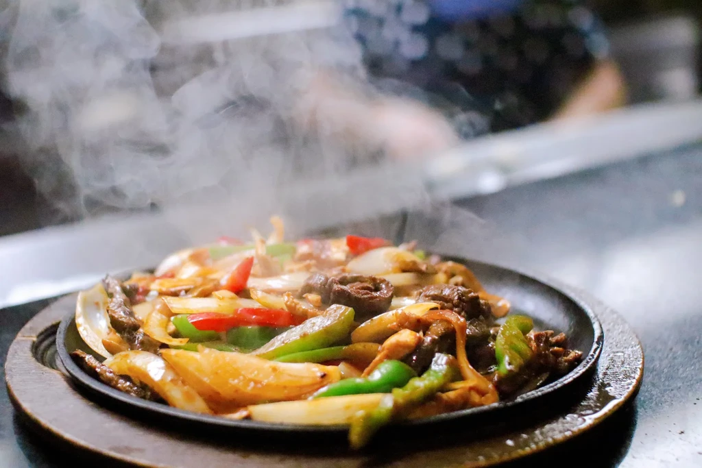 Steaming fajitas with beef, onions, and peppers on a sizzling plate.