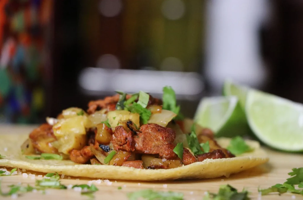 Close-up of a corn tortilla taco with meat, pineapple, cilantro, and lime.