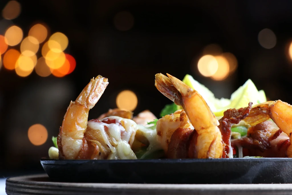 Two bacon-wrapped shrimp with cheese and lime in a dark setting.