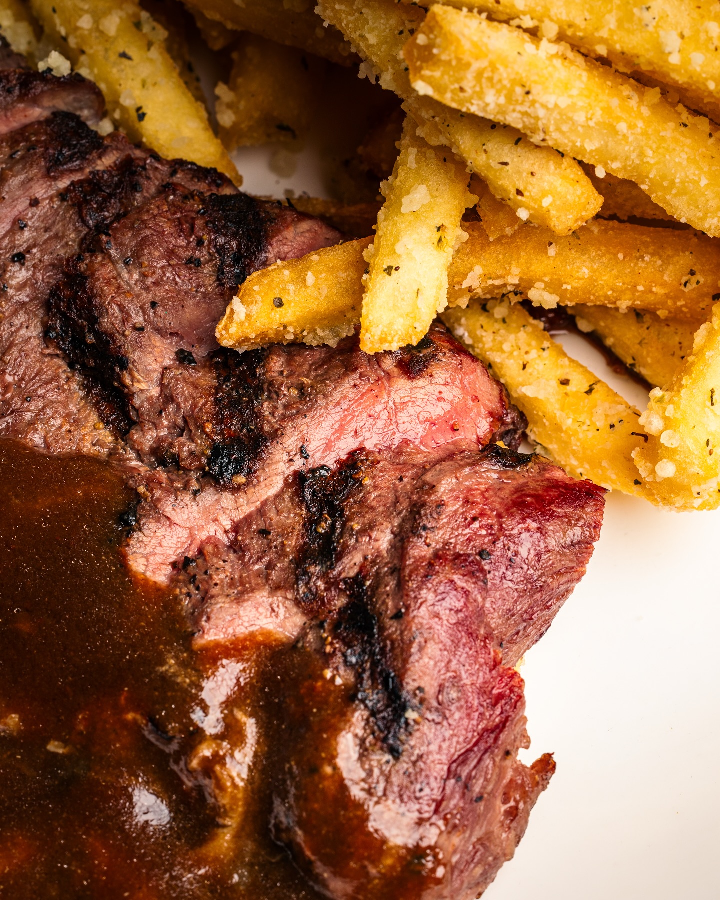 Grilled steak slices with brown sauce and seasoned french fries.
