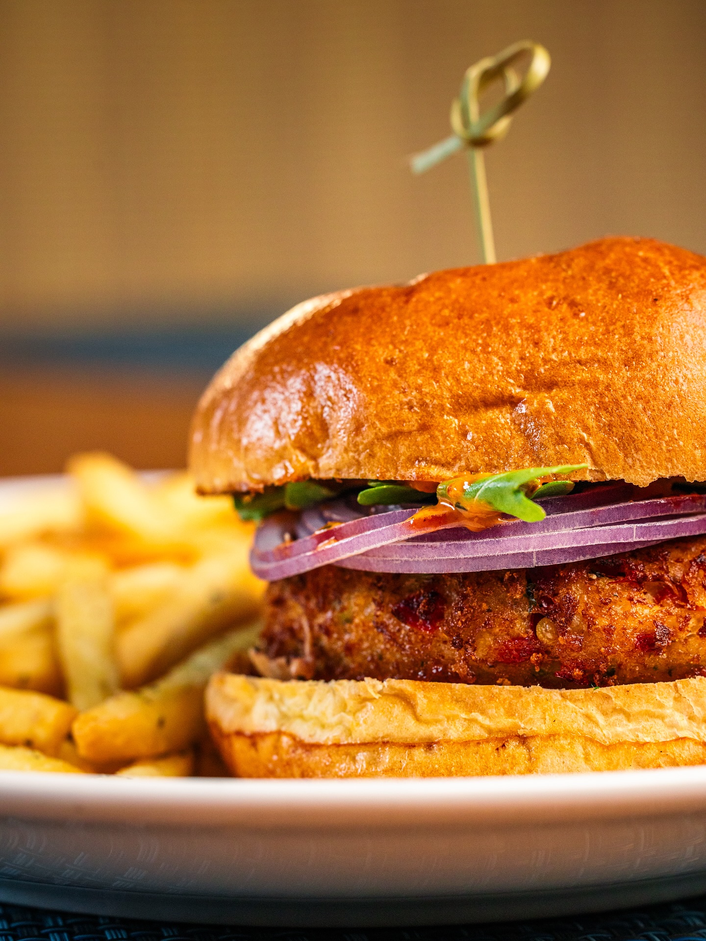 Close-up of a burger with red onion, green garnish, and fries.