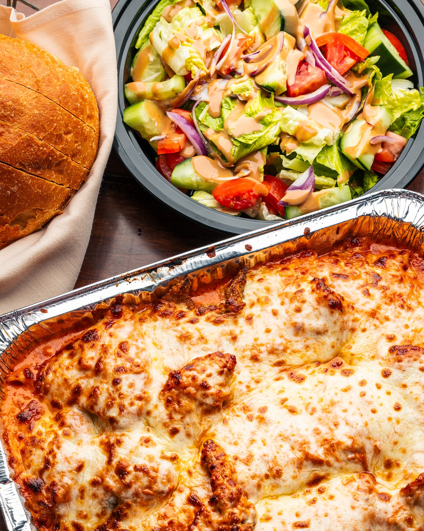 Tray of baked pasta with cheese, side salad, and bread.
