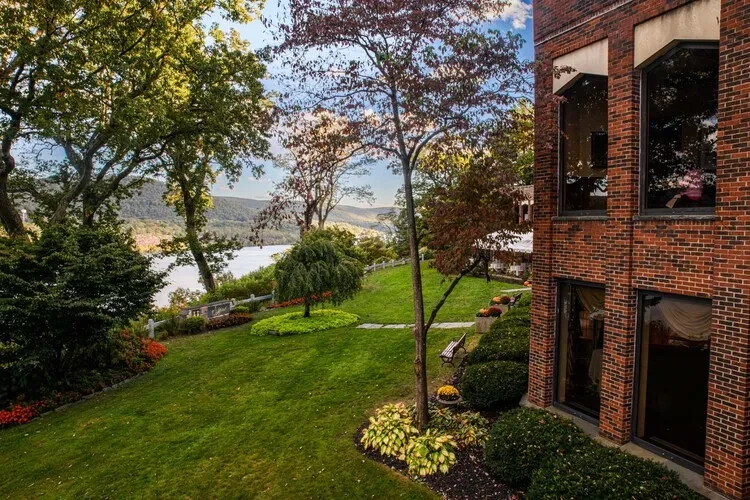 Large red brick house overlooking a hilly green garden and lake.