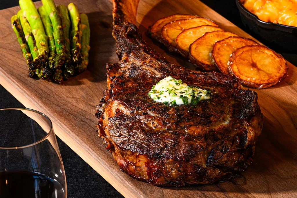 Tomahawk steak, roasted asparagus, and potatoes on a wooden board.
