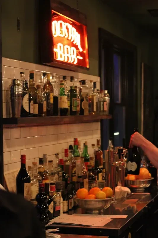 A dimly lit "COCKTAIL BAR" sign hangs over a well-stocked bar.