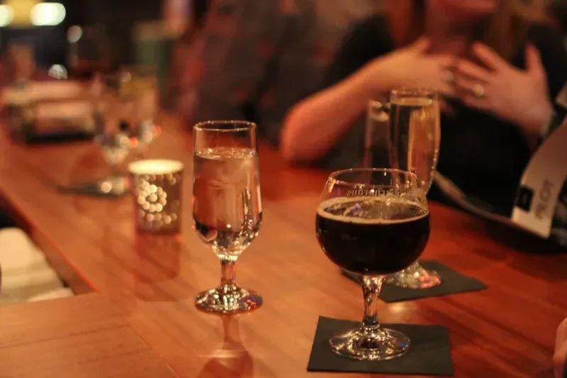 A water glass and beer glass sit on a shiny wooden bar.