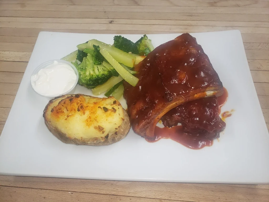 BBQ ribs, twice-baked potato, steamed green vegetables on a white plate.