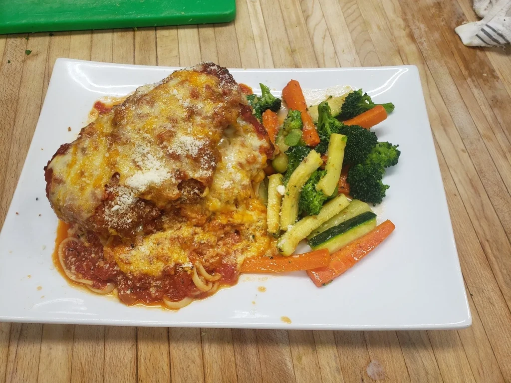 Fried cutlet with melted mozzarella, tomato sauce, pasta, and vegetables.