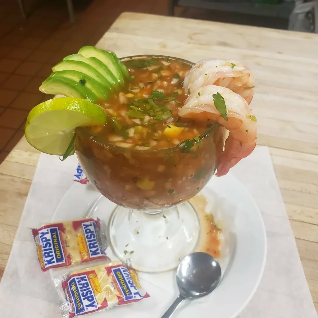 Close-up of shrimp cocktail with avocado, lime, crackers, and spoon.