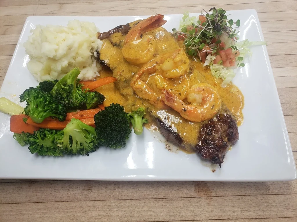 Steak and shrimp with creamy sauce, mashed potatoes, and steamed vegetables.