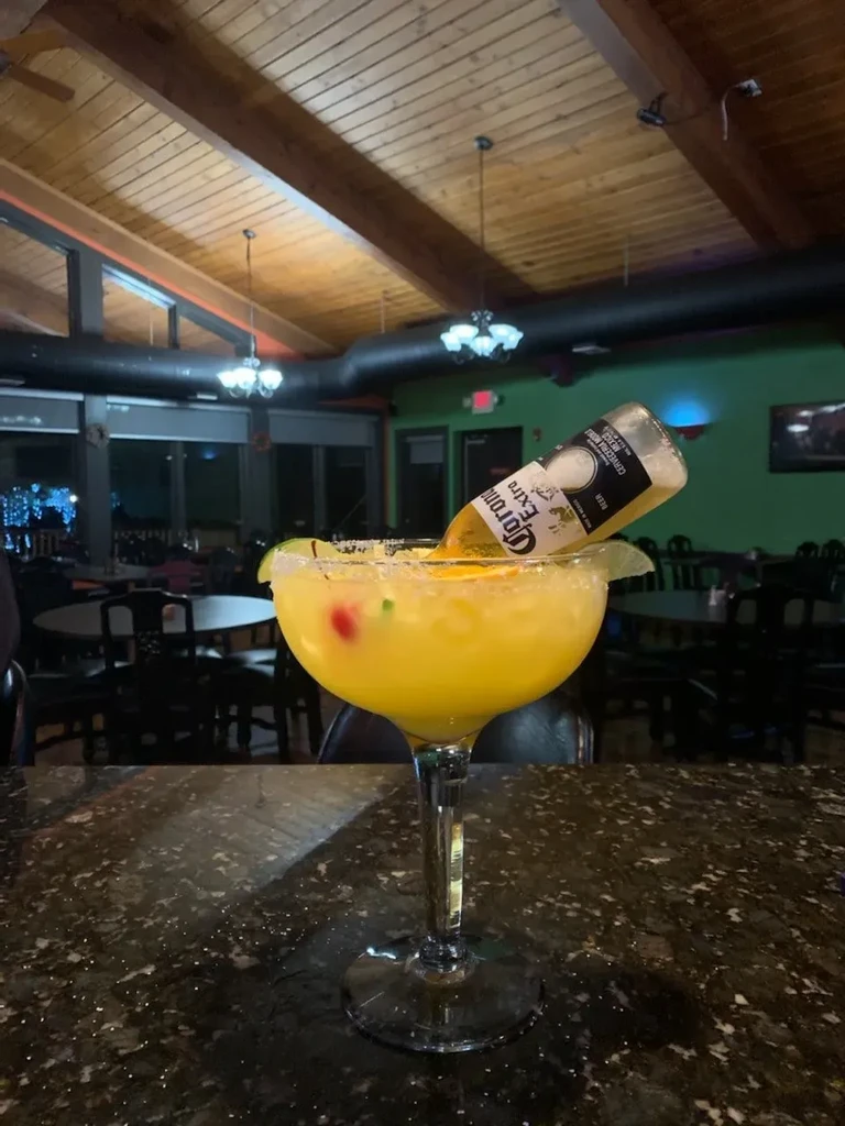 Margarita glass with yellow drink, lime, and submerged Corona beer bottle.