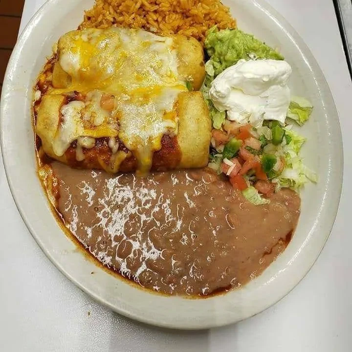 Plate of cheesy enchiladas, rice, refried beans, guacamole, and sour cream.