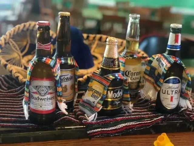 Five beer bottles, serape-decorated, on a striped surface with a sombrero.