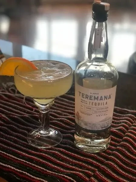Teremana Blanco tequila bottle and frothy yellow cocktail with orange garnish.