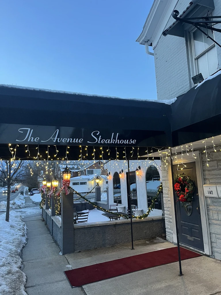 Snowy exterior of The Avenue Steakhouse at night with festive lights.