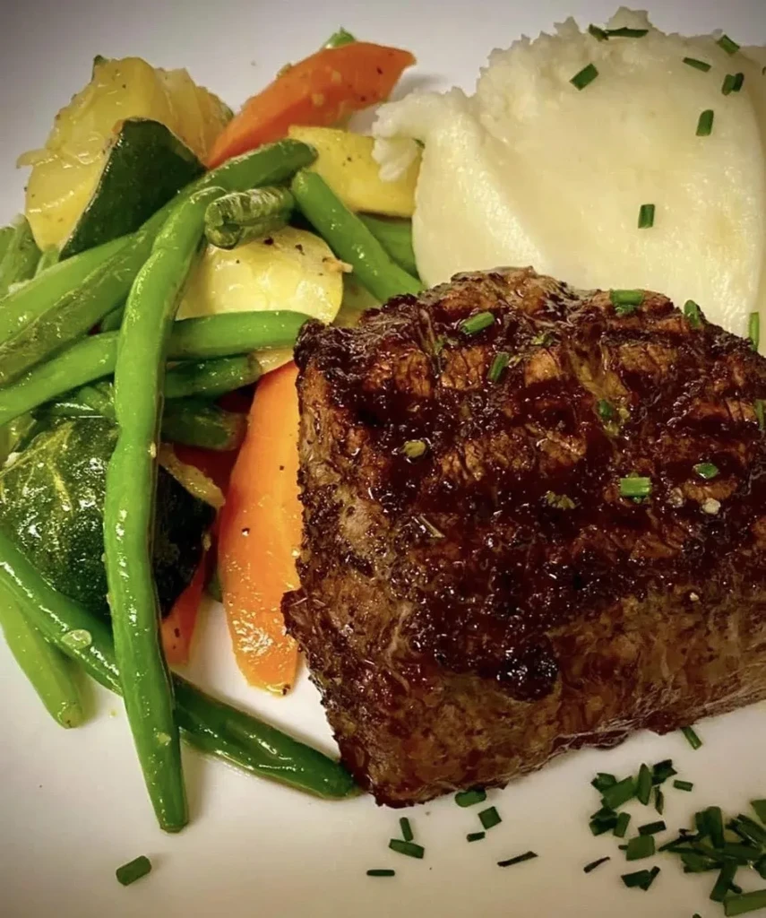 Close-up of plated steak, mixed vegetables, and mashed potatoes.