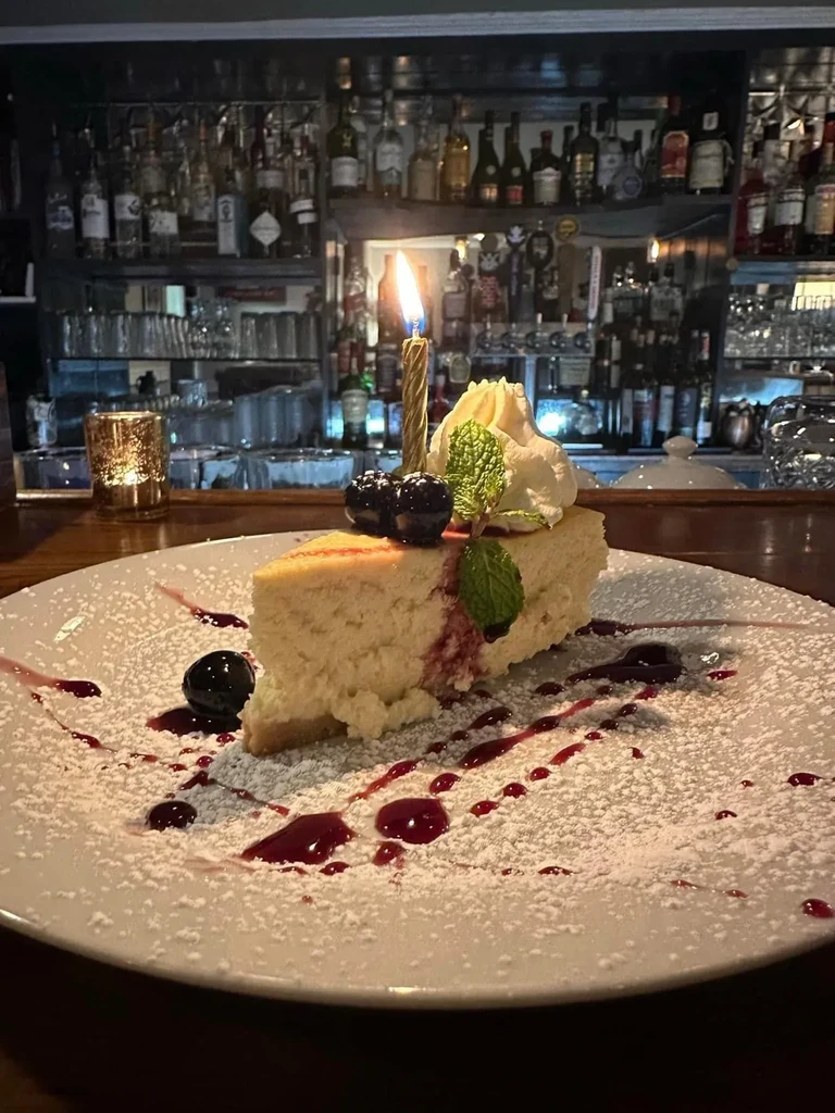 Birthday cheesecake with berries and a lit candle at a bar.