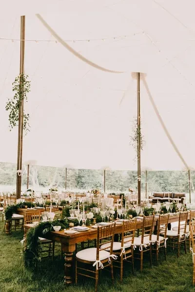 A rustic outdoor reception setup with long wooden tables under a white tent.