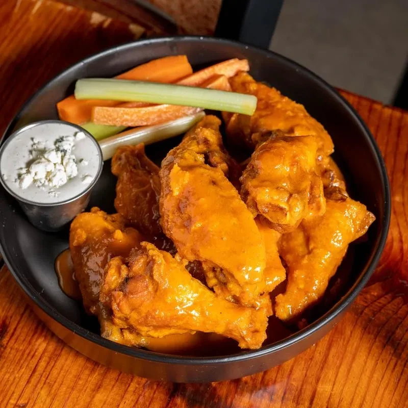 Orange buffalo wings, blue cheese dip, celery, and carrot sticks.
