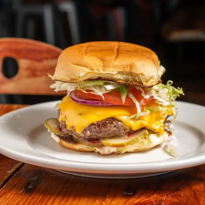 Cheeseburger with melted cheddar, lettuce, tomato, onion, and pickles on a plate.