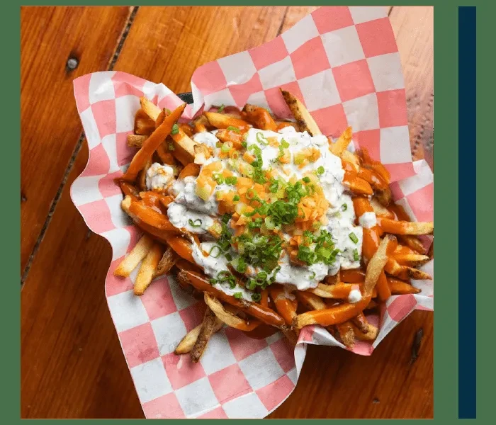 Top-down view of loaded fries with sauces, green onions, and orange vegetables.