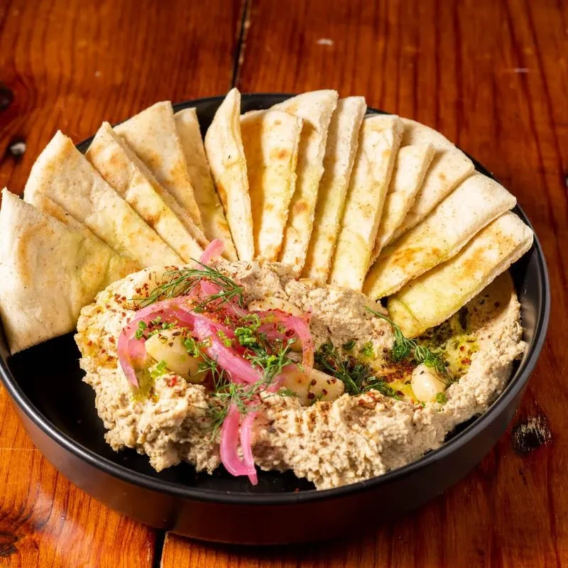 Plated hummus with roasted garlic, pickled onions, dill, and fanned pita.