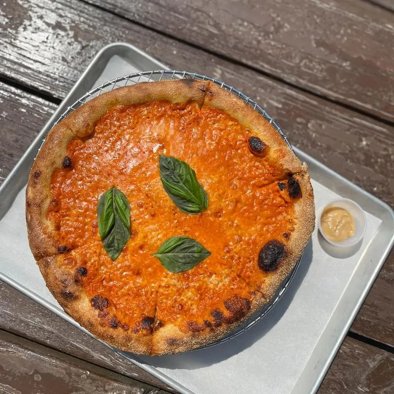 Sliced pizza, golden crust, red sauce, basil, with dipping sauce.