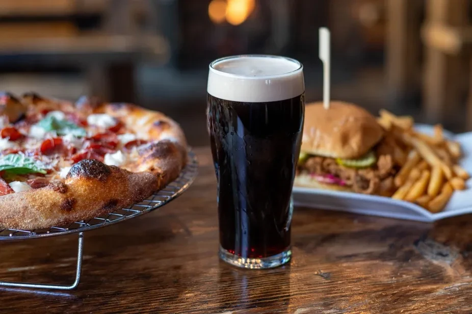 Pepperoni pizza, dark beer, and burger with fries on a table.