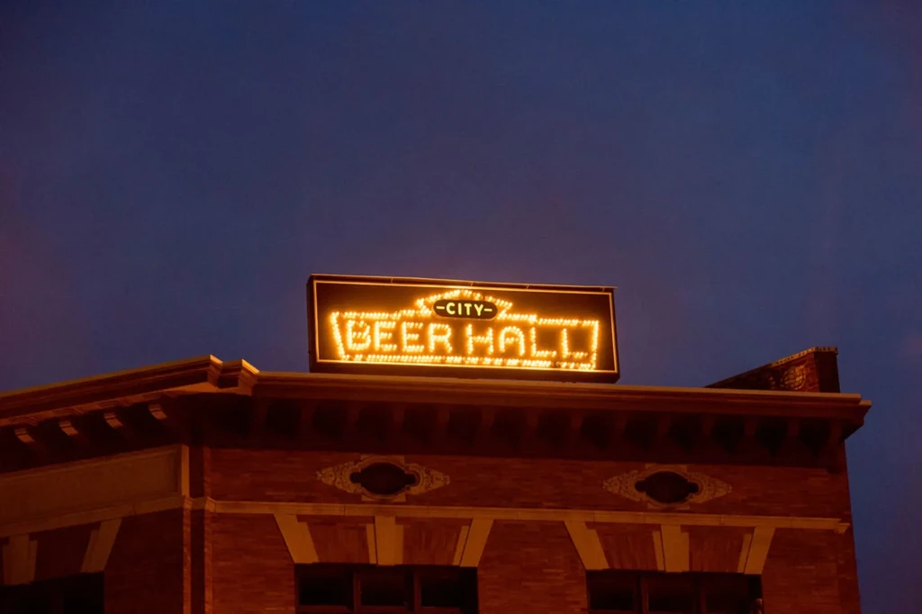 Glowing "CITY BEER HALL" sign on a red brick building at night.