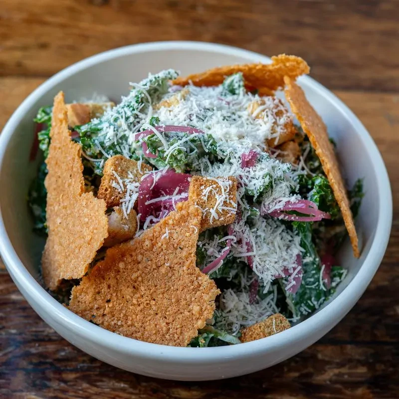 Close-up of kale salad with red onion, croutons, cheese, and crisps.