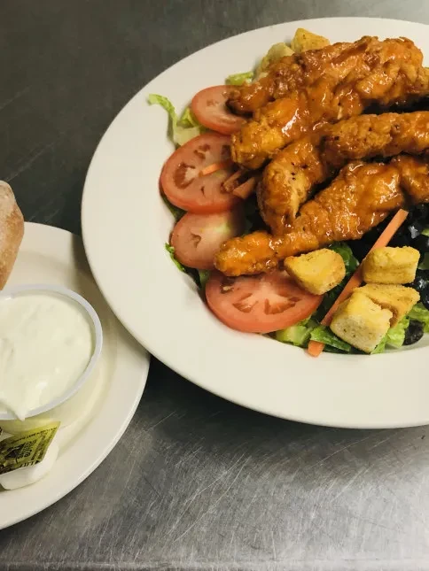 Close-up of a chicken tender salad with bread and dipping sauce.