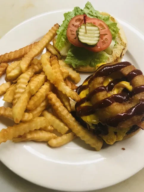Overhead close-up of a cheeseburger with onion rings and crinkle-cut fries.