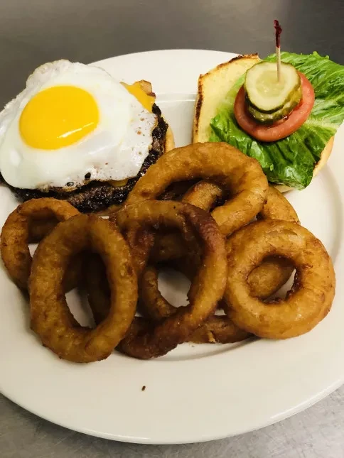 Burger with egg, cheese, lettuce, tomato, pickle, and crispy onion rings.
