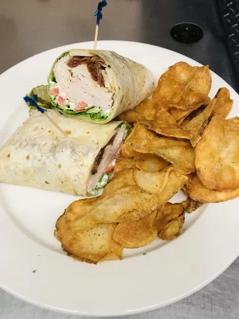 White plate with cut turkey-bacon wrap, lettuce, tomato, chips, and dressing.