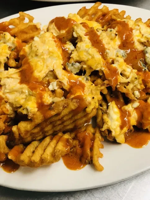 Waffle fries with melted cheese and reddish-orange sauce on a plate.