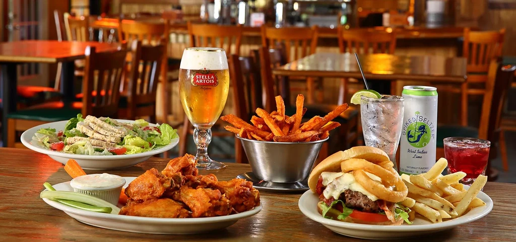 Restaurant table laden with wings, salad, burger, fries, beer, and seltzer.