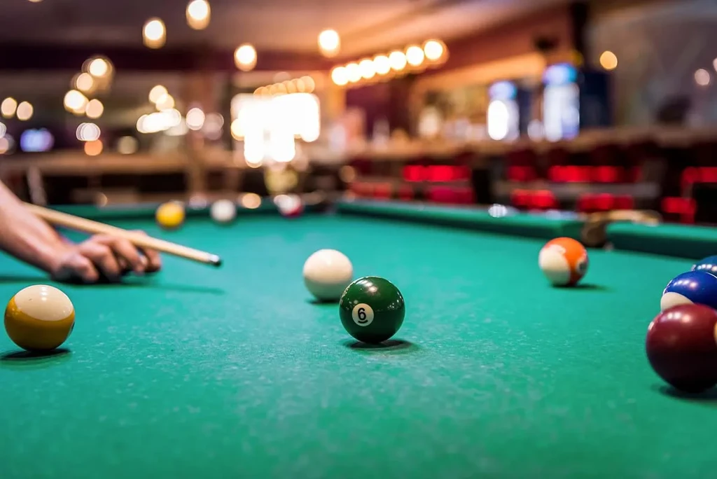 Close-up: Hands poised to strike cue ball on green felt pool table.