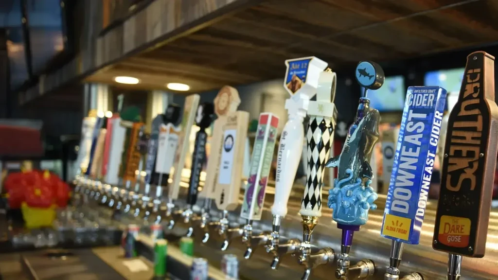 A row of diverse, labeled beer and cider taps at a bar.