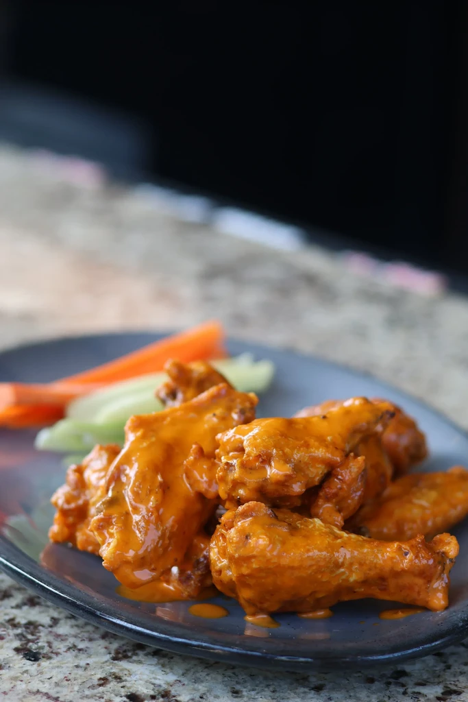 Plate of orange-sauced buffalo wings with celery and carrot sticks.