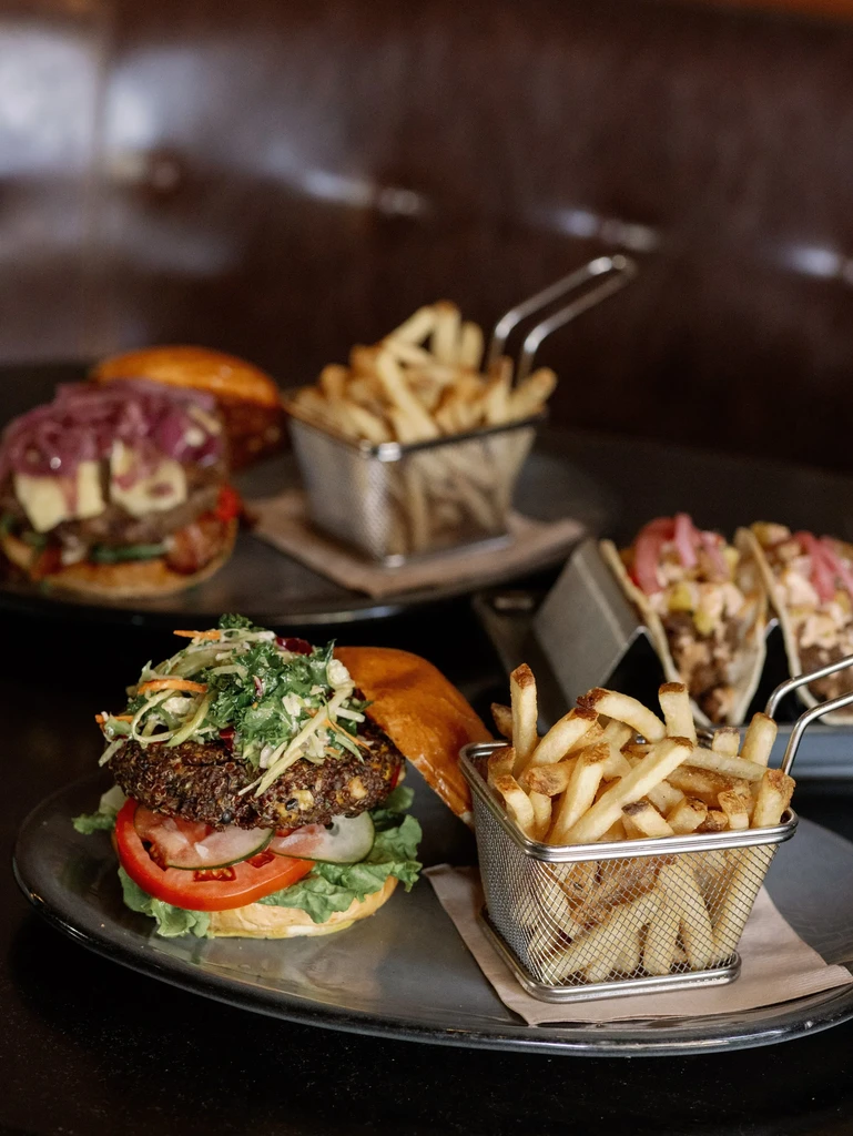 Gourmet burger, fries, and colorful tacos on a dark table.