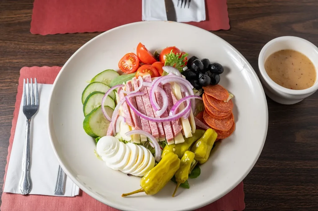 Assorted colorful salad in a white bowl with dressing on wooden table.