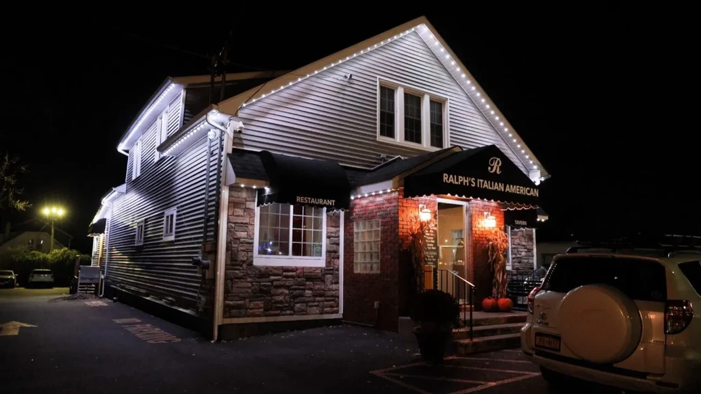 Illuminated Ralph's Italian American restaurant at night, string lights, pumpkins.