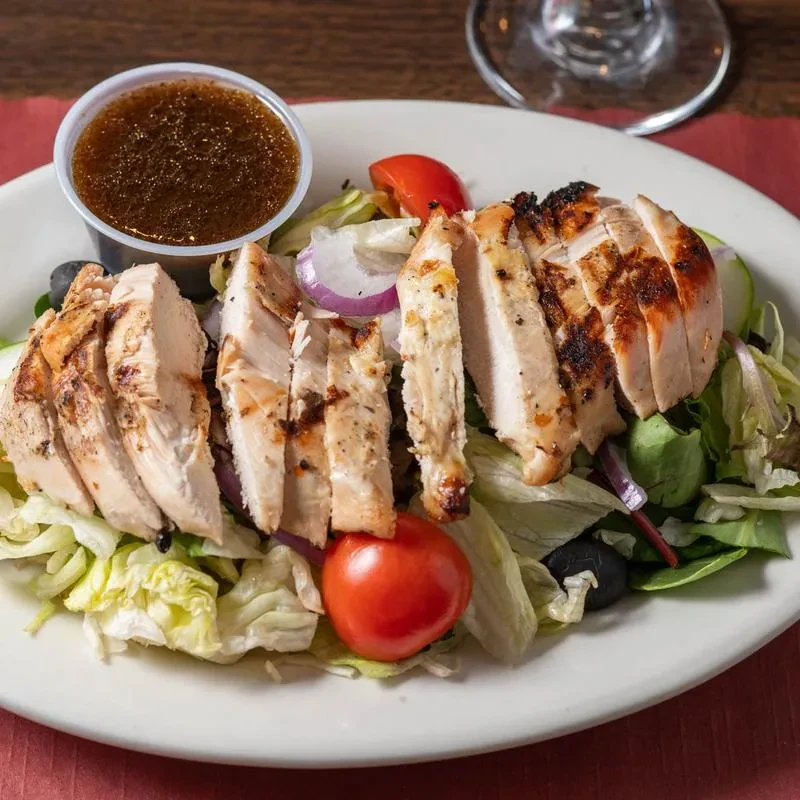 Overhead shot of grilled chicken salad with dressing cup.