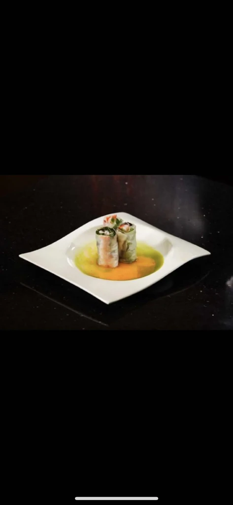 Two spring rolls with shrimp, greens, yellow sauce on white plate.