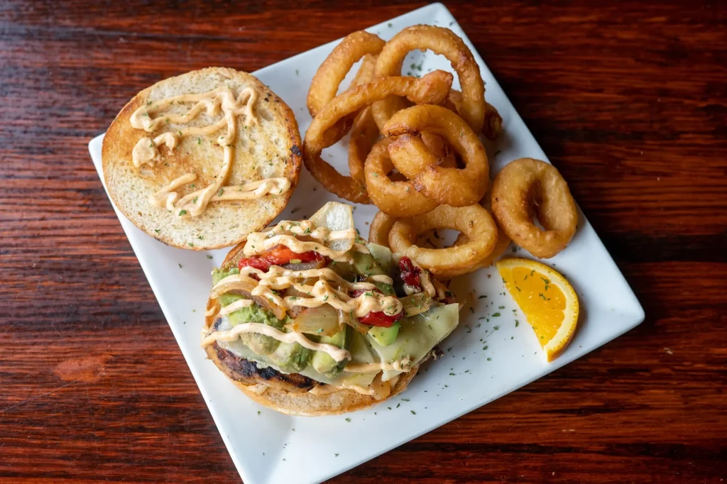 Open-faced sandwich with meat, avocado, cheese, creamy orange sauce, onion rings.