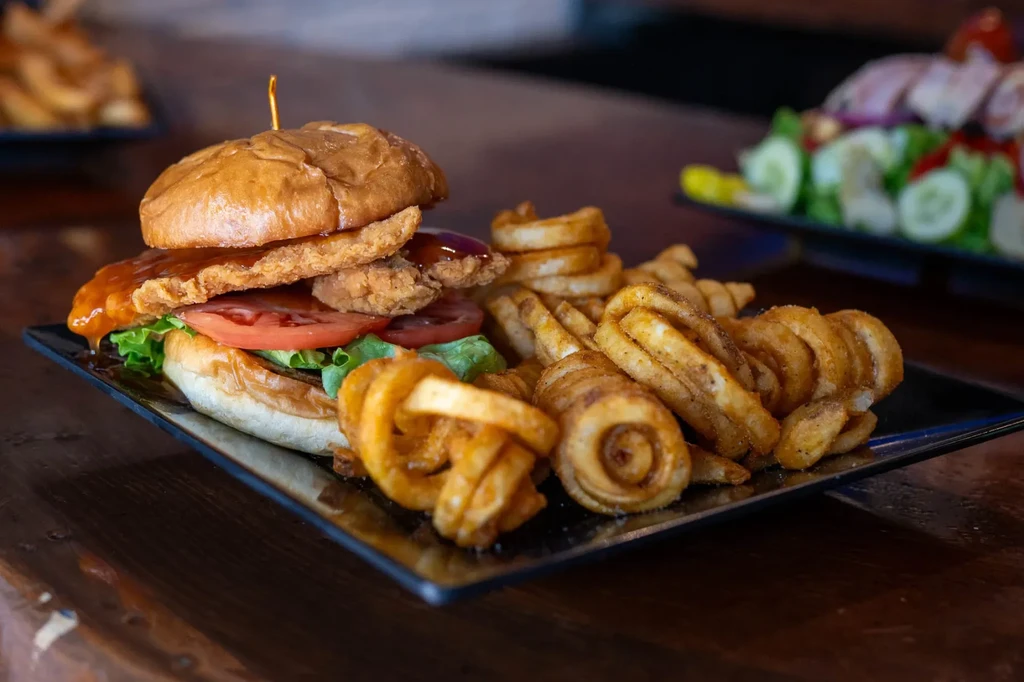 Crispy chicken sandwich with sauce, lettuce, tomato, and seasoned curly fries.