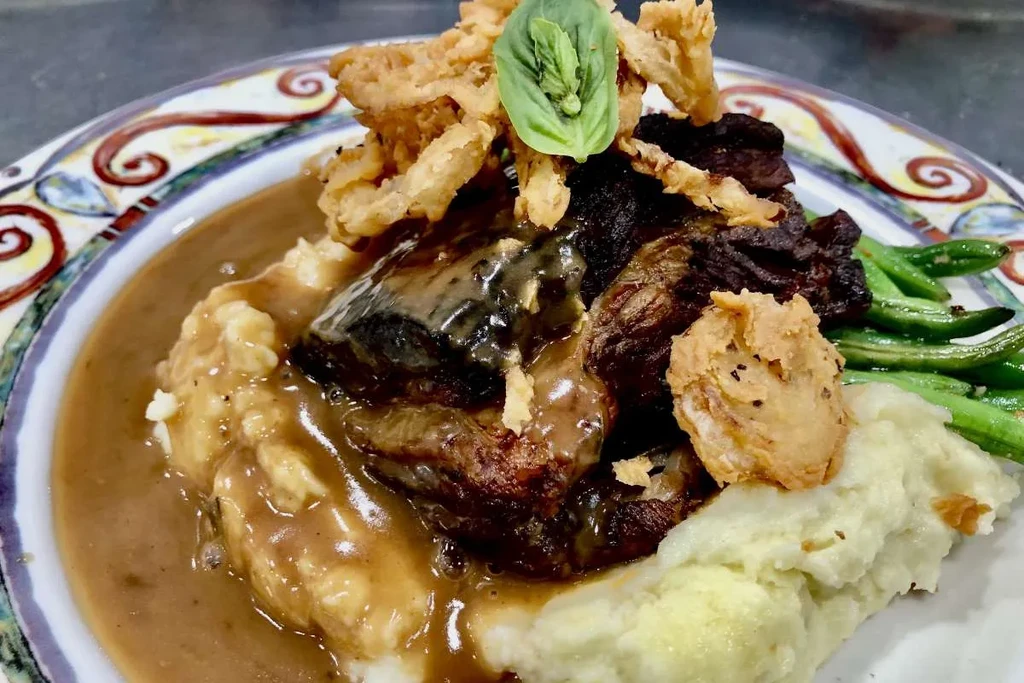 Braised meat, mashed potatoes, gravy, fried onions, basil, and string beans.