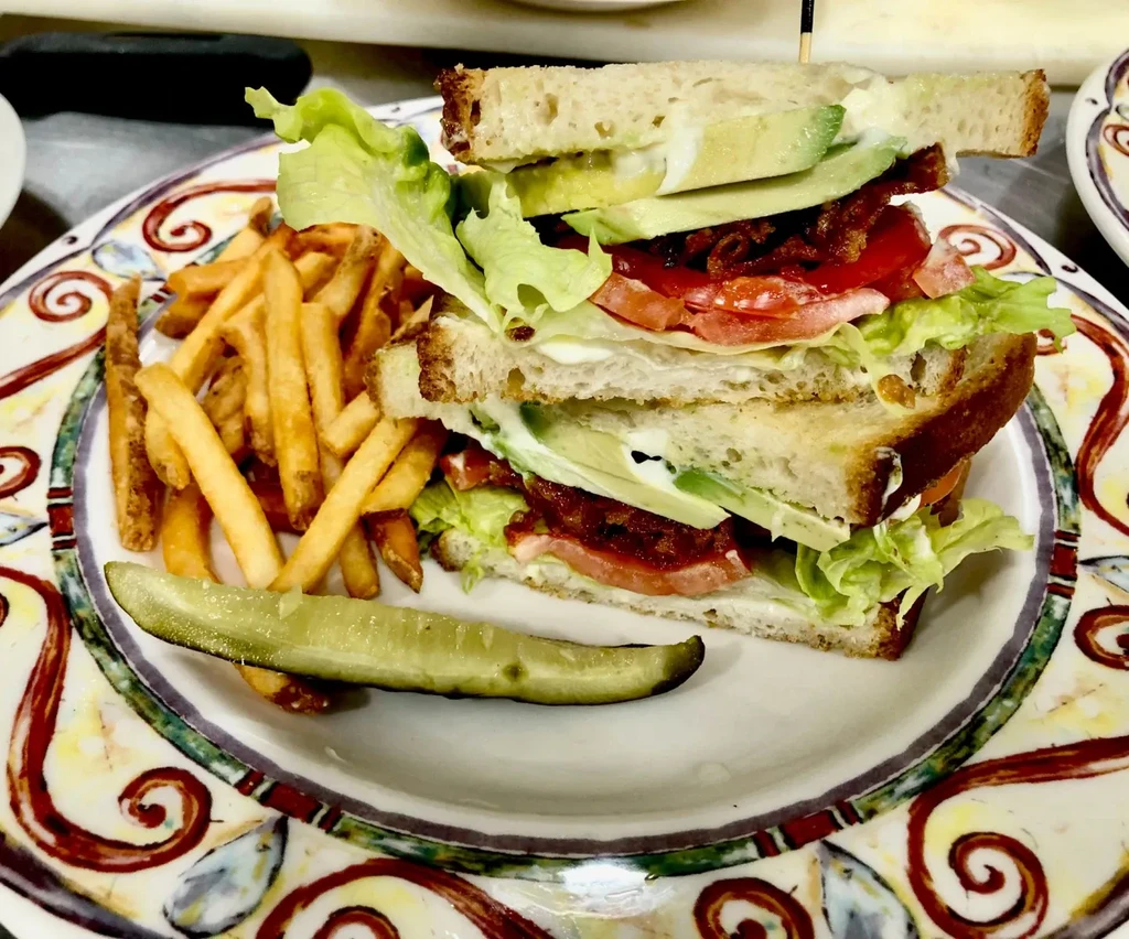 Close-up of a hearty club sandwich, french fries, and pickle.